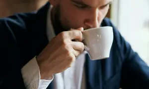 En man i kostym tar en klunk kaffe ur en vit kopp. Kanske blir man pigg av kaffe.