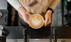 Barista håller en vacker latte med latte art. Undrar hur många koppar kaffe per paket Zoegas det blir?