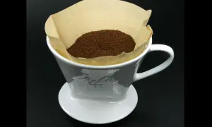 En vit kaffefilterhållare med kaffepulver i ett pappersfilter. Vem uppfann kaffefiltret? Melitta Bentz 1908.