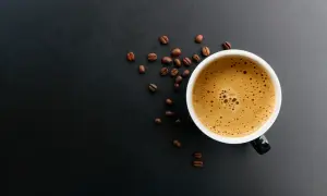 En kopp kaffe med skummig yta och kaffebönor runt omkring. Kanske någon som har en vegan i kaffet idag?