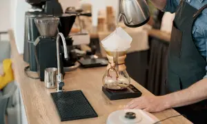 Barista häller vatten över kaffefilter i en Chemex. En kaffekvarn och en kran syns i bakgrunden. Intressant kaffe fakta!