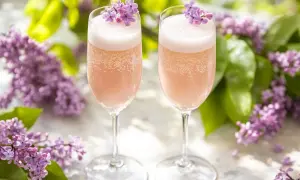Två glas med rosa bubbel, dekorerade med syrenblommor. Perfekt för ett syrensirap recept en solig dag.