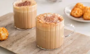 Två glas med krämiga kaffedrinkar, toppade med kanel och en liten tallrik med makroner. Perfekt för inspiration till egna kaffedrinkar recept.