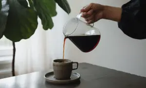 En hand häller upp mörkt kaffe från en glaskanna i en mugg. En fin stund för att njuta av kaffe, inte espresso.