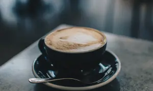 En kopp cappuccino latte med vacker skumkonst på en mörk tallrik med en sked.