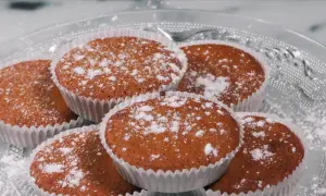 En hög med glutenfria saffransmuffins, pudrade med florsocker, ligger på ett vackert glasfat. Perfekt för fikat!