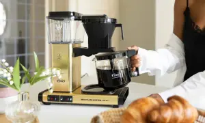 En guldfärgad Moccamaster kaffebryggare med en glaskanna fylld med kaffe. Denna modell är känd för sin optimala bryggtemperatur.