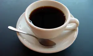 En vit kopp med mörkt kaffe och en sked på en fat. En påminnelse om kaffe ursprung och dess resa till din kopp.