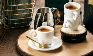 Enkel espresso med gyllene sked och mjölkkanna. Två koppar står staplade på träbitar.