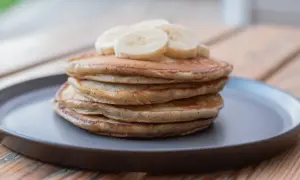 En hög med fluffiga bananpannkakor, toppad med bananskivor. Ett enkelt och gott bananpannkaka recept för frukost eller mellanmål.