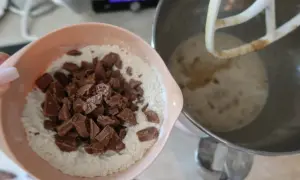 En skål med mjöl och chokladbitar för en saftig banankaka med choklad. Bredvid står en köksmaskin med smet.