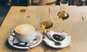 En kopp cappuccino med hjärtkonst, två glas avec och en skål med sylt. Perfekt avec till kaffet.