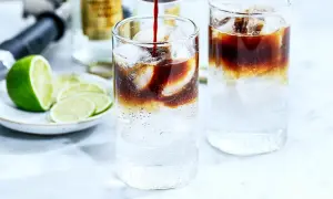 Två glas med kaffe tonic, is och lime. En flaska och en limeklyfta i bakgrunden.