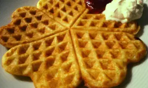 Golden-brown heart-shaped waffles with jam and whipped cream.