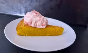 En bit glutenfri saffranskladdkaka med vit choklad, toppad med rosa grädde.