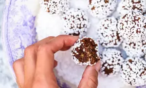 En hand håller en bit av lyxiga chokladbollar, rullade i vita pärlsocker.