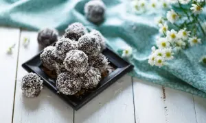 En hög med chokladbollar, perfekta för chokladbollens dag, rullade i kokosflingor. Blommor och en turkos duk i bakgrunden.