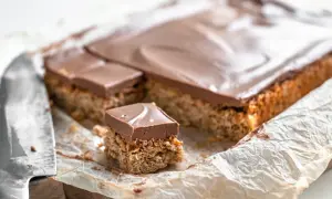 En bit av en kaka med chokladöverdrag, som ser ut att vara nougatrutor glutenfria, ligger på bakplåtspapper bredvid en kniv.