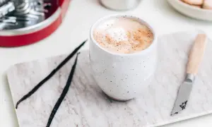 En krämig vaniljlatte hemma, med vaniljstänger och en liten kniv på en marmorerad bricka.