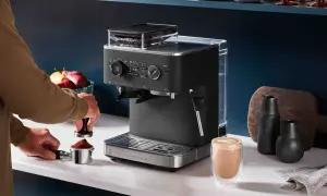 En person förbereder espresso i en kaffebryggare. En färdigbryggd latte står bredvid.