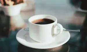En kopp med **temp rostas** kaffe står på ett fat. I bakgrunden syns en skål med kex.