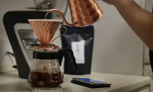 En person häller varmt vatten över kaffepulver i en kopparfilterhållare för att brygga kaffe manuellt.