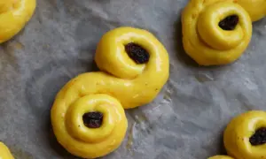 Gyllene, S-formade glutenfria bullar med russin på bakplåtspapper. Perfekt för fikat!