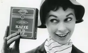 En kvinna med hatt och randig scarf håller upp en låda Löfbergs Kaffe. Kanske hon vet vilka som dricker mest kaffe i Sverige?