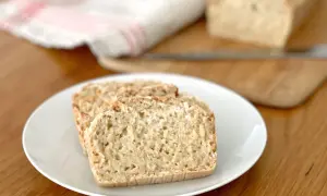Tre skivor glutenfri limpa på en vit tallrik. En hel limpa syns i bakgrunden.