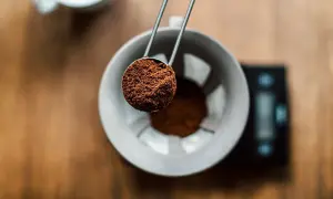 Malen kaffepulver hälls från en skopa ner i en filterhållare, redo för bryggning. Rätt kaffe temperatur är avgörande för smaken.