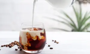 Mjölk hälls i ett glas med iskaffe och kaffebönor, en perfekt islatte.