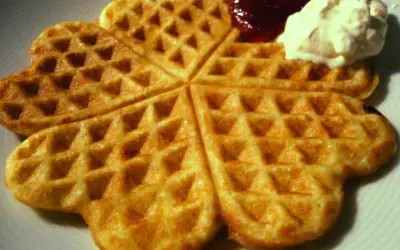 Golden-brown heart-shaped waffles with jam and whipped cream.