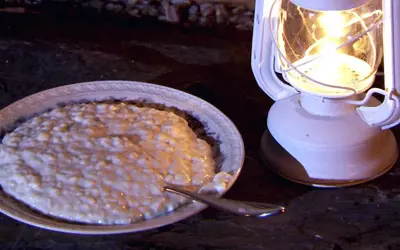En skål med krämig risgrynspudding med bittermandel, belyst av en vit oljelampa.