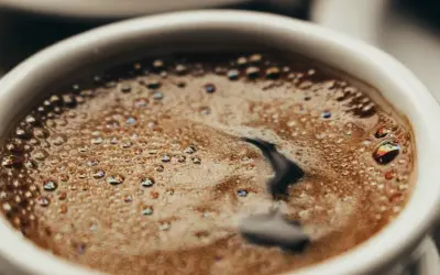 En vit kopp med bubbligt java kaffe. Skummet har regnbågsskimrande bubblor och en mörk virvel i mitten.