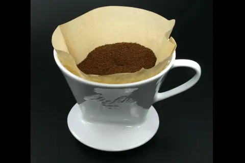 En vit kaffefilterhållare med kaffepulver i ett pappersfilter. Vem uppfann kaffefiltret? Melitta Bentz 1908.