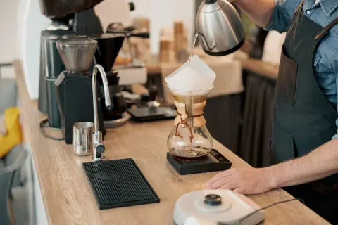 Barista häller vatten över kaffefilter i en Chemex. En kaffekvarn och en kran syns i bakgrunden. Intressant kaffe fakta!