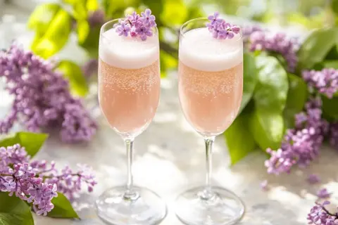 Två glas med rosa bubbel, dekorerade med syrenblommor. Perfekt för ett syrensirap recept en solig dag.