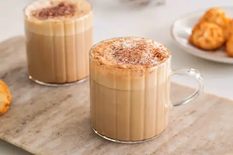Två glas med krämiga kaffedrinkar, toppade med kanel och en liten tallrik med makroner. Perfekt för inspiration till egna kaffedrinkar recept.