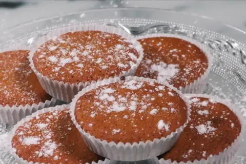 En hög med glutenfria saffransmuffins, pudrade med florsocker, ligger på ett vackert glasfat. Perfekt för fikat!