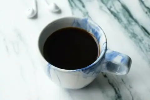 En kopp kaffe, perfekt för att njuta av ditt americano recept. Vita hörlurar ligger bredvid.