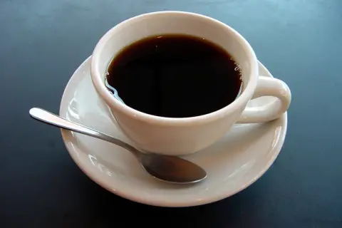 En vit kopp med mörkt kaffe och en sked på en fat. En påminnelse om kaffe ursprung och dess resa till din kopp.