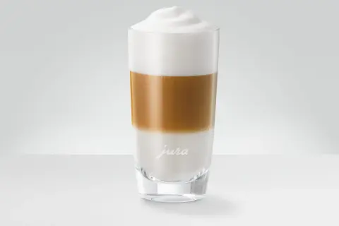 En perfekt lagerdelad latte macchiato i ett glas med Jura-logotyp.