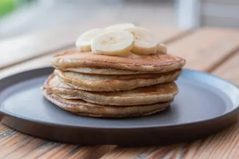 En hög med fluffiga bananpannkakor, toppad med bananskivor. Ett enkelt och gott bananpannkaka recept för frukost eller mellanmål.