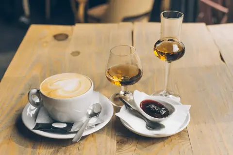 En kopp cappuccino med hjärtkonst, två glas avec och en skål med sylt. Perfekt avec till kaffet.