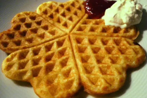 Golden-brown heart-shaped waffles with jam and whipped cream.
