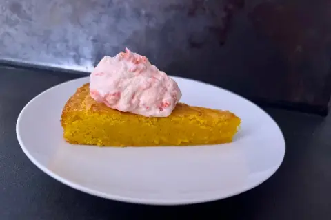 En bit glutenfri saffranskladdkaka med vit choklad, toppad med rosa grädde.