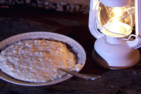 En skål med krämig risgrynspudding med bittermandel, belyst av en vit oljelampa.