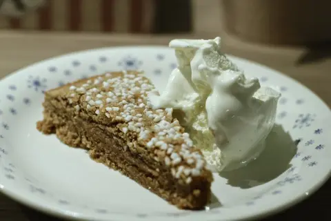 En bit glutenfri kanelbullekladdkaka med en kula vaniljglass på en tallrik med blå blommor.