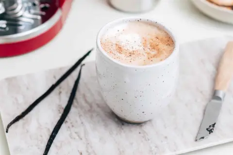 En krämig vaniljlatte hemma, med vaniljstänger och en liten kniv på en marmorerad bricka.