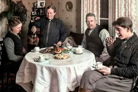 En familj samlas runt ett dukat bord för att dricka kaffe. En kvinna häller upp kaffe, en annan tittar ner, medan två män sitter och samtalar. En scen som speglar kaffe historia i Sverige.